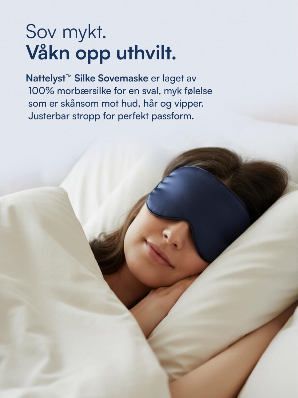 Kvinne sover fredfullt med mørk blå silke sovemaske, innpakket i hvitt sengetøy