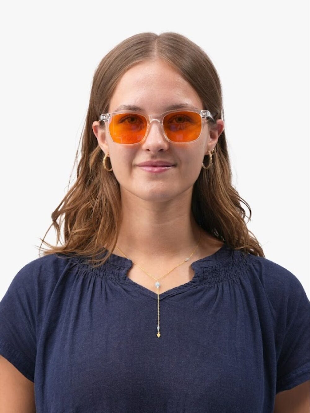Kvinde i klarstel blålysbriller med orange linser, navy bluse, guldøreringe og fint lariat-halskæde