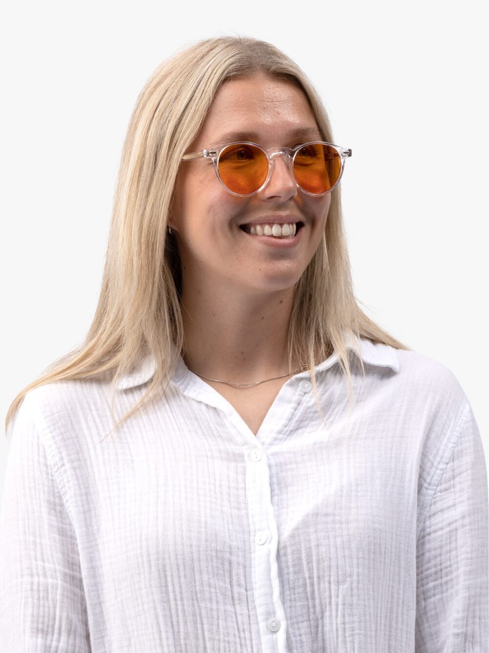 Smilende kvinde med langt blondt hår, gennemsigtige stelbriller med orange linser og hvid løstsiddende skjorte