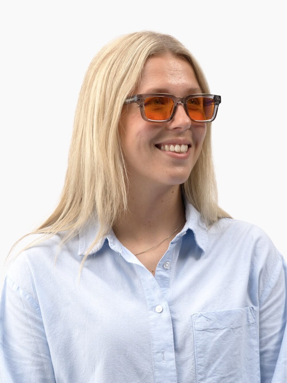Smilende kvinde med blondt hår, grå stel solbriller med orange glas og lyseblå skjorte, blik mod højre