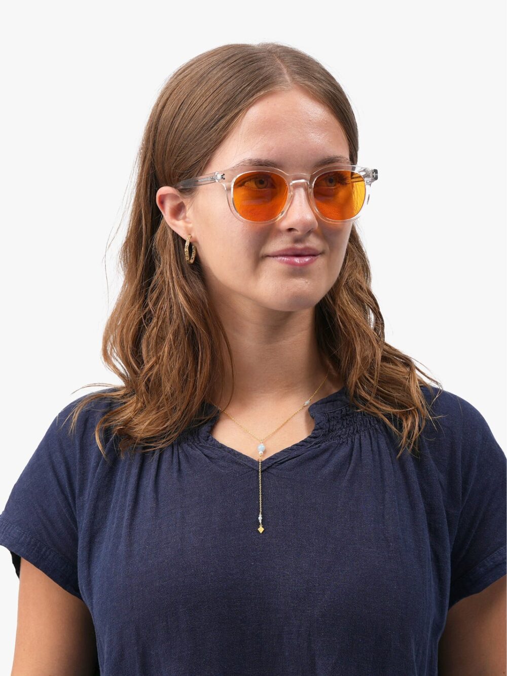 Kvinde med gennemsigtige solbriller med orange linser, navy bluse og gyldent halskædevedhæng