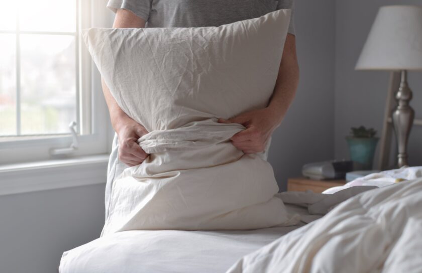 Woman putting a white pillowcase on a pillow while making the bed by a window